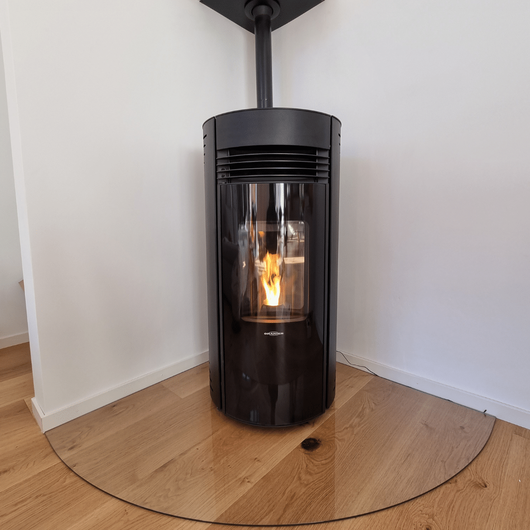 Poêle à granulés noir moderne avec protection en verre et feu allumé.