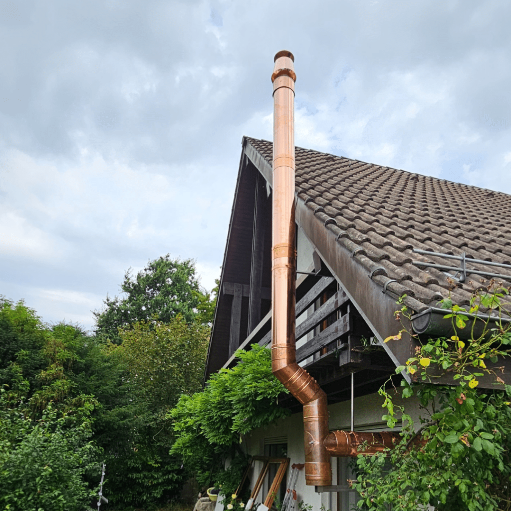 Conduit de cheminée en cuivre brillant installé sur une maison avec toiture en tuiles.