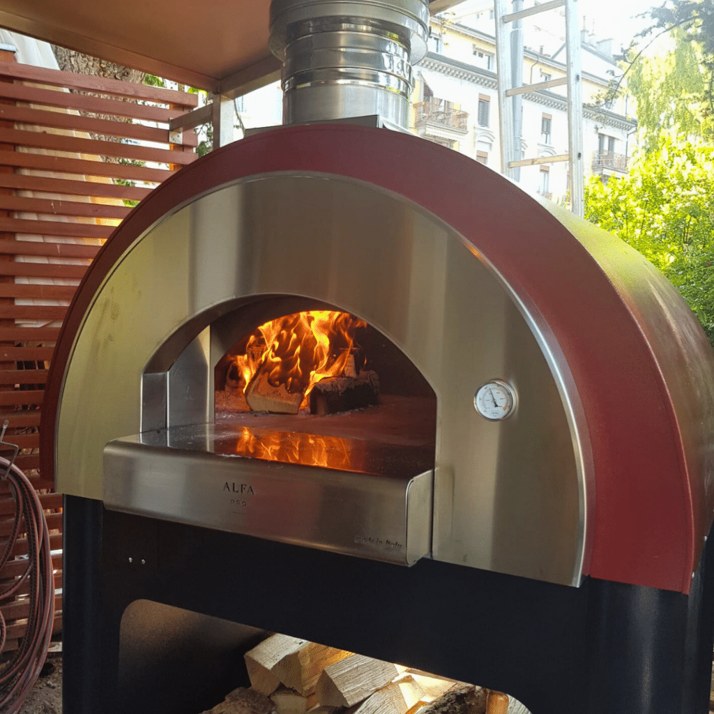 Four à bois avec façade en acier inoxydable et feu allumé, conçu pour la cuisson des pizzas.