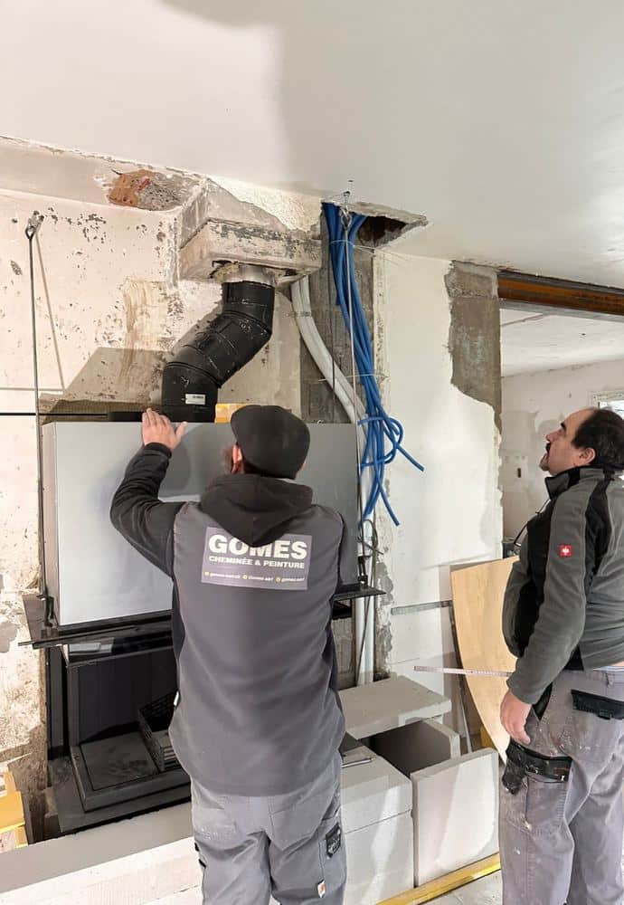 Deux poêliers-fumistes de Gomes installent un insert et raccordent le conduit de fumée sur un chantier à Genève