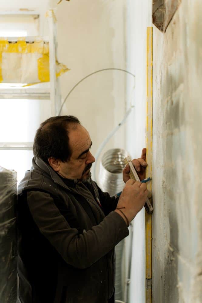Poêlier-fumiste de Gomes prenant les mesures au mur avant la pose d'un conduit flexible pour poêle à bois