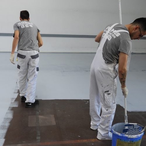 Deux peintres de Gomes SARL appliquent de la peinture au sol dans une blanchisserie à Genève.